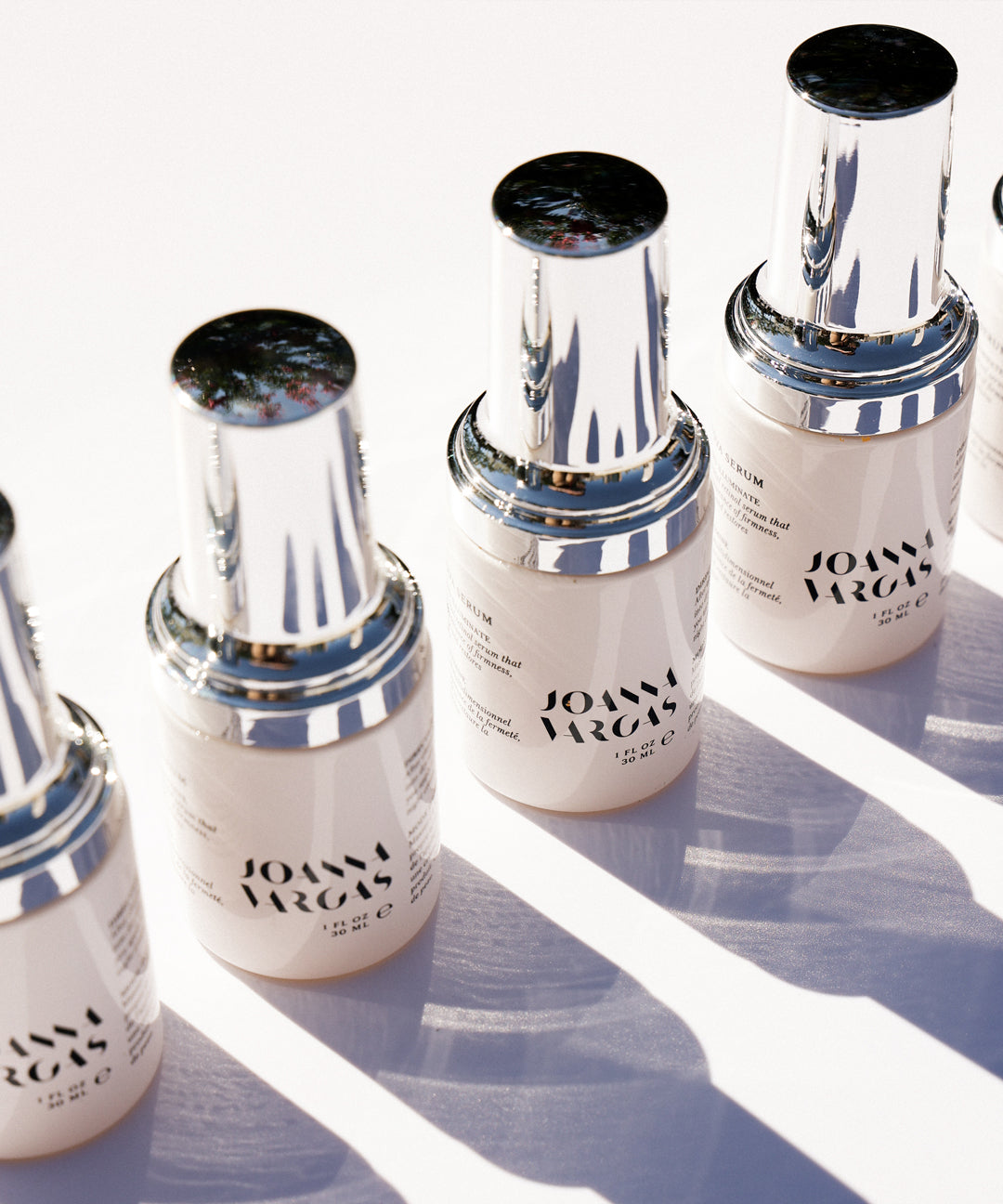 Three bottles of Joah Marcus serum with cream-colored liquid, metallic silver bands, and black caps arranged in a row.
